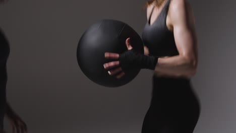 Studioaufnahme-Von-Zwei-Reifen-Frauen-In-Fitnessstudio-Fitnesskleidung,-Die-Gemeinsam-Mit-Einem-Gewichteten-Medizinball-Trainieren